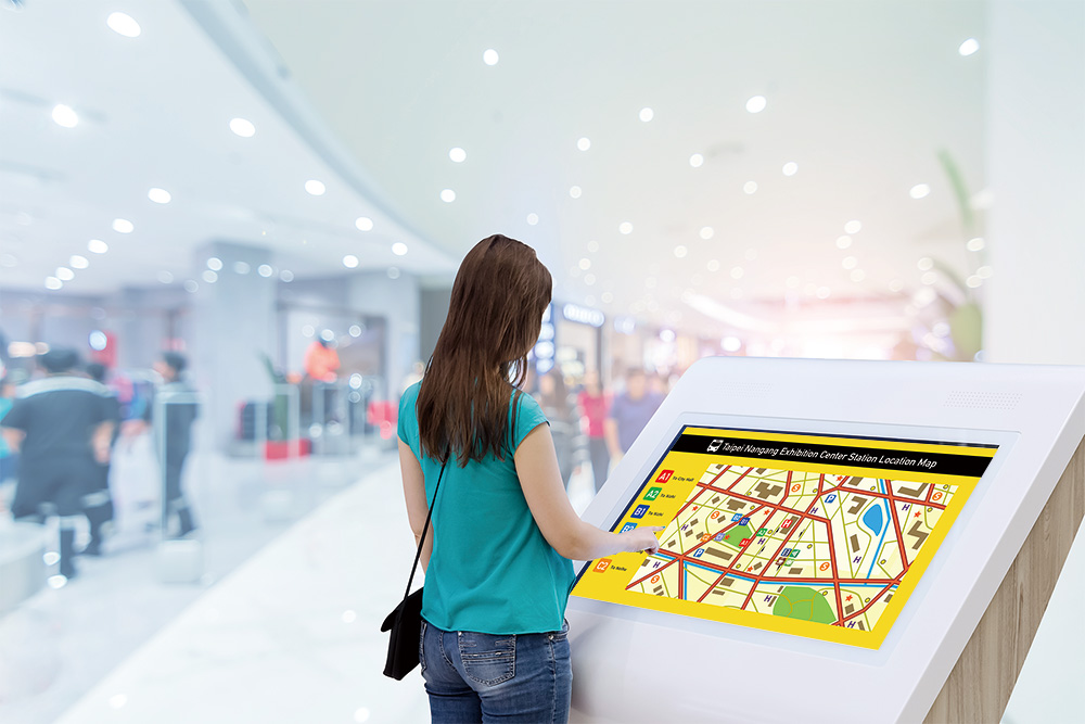 A female touching a digital wayfinding signage showing map info.